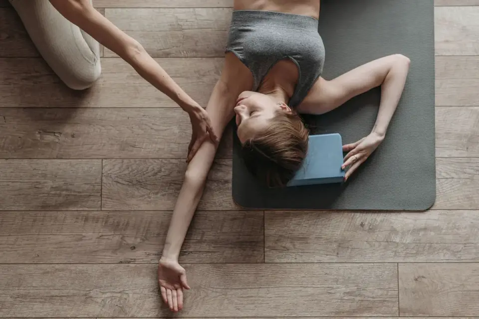 A dog lying calmly on a padded mat during a physical therapy session with a person supporting its leg